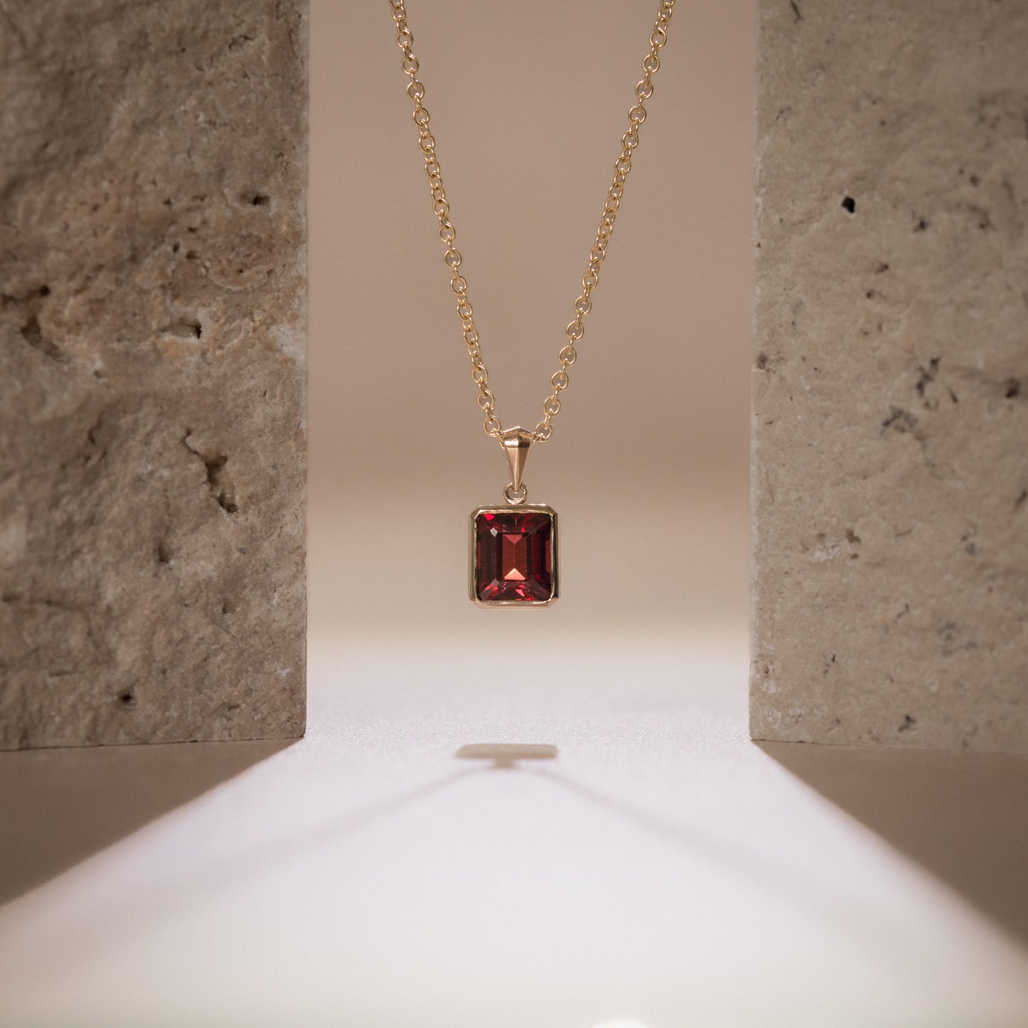 Gold necklace with a garnet gemstone pendant on a neutral background
