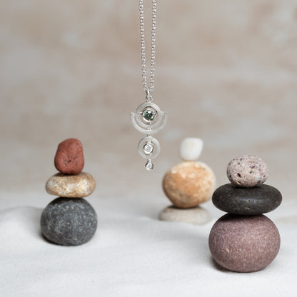 Silver necklace with a diamond pendant on a background of stacked stones