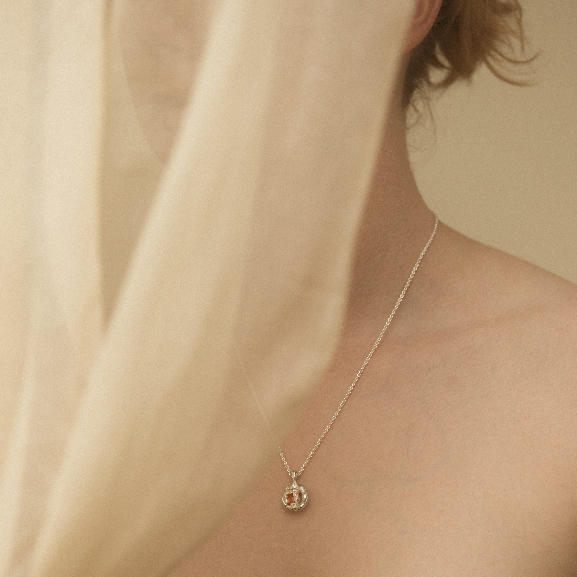Silver necklace with a sapphire pendant worn by a person against a neutral background