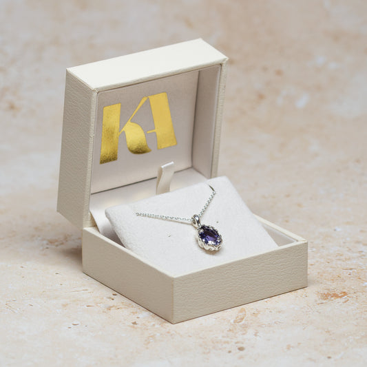 Sterling silver and oval iolite pendant necklace pictured in a pendant box with Kate Archer branding on a neutral background.