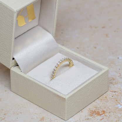 An 18cy yellow gold eternity ring set with 2mm lab-grown diamonds, displayed inside an open cream-colored textured jewelry box on a light beige stone surface.