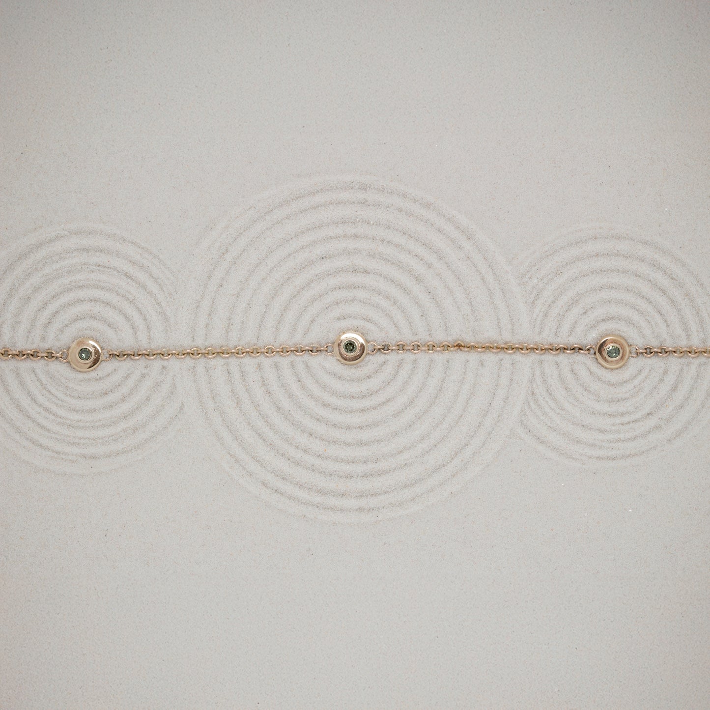 Delicate gold bracelet with small green diamonds on a textured sand background
