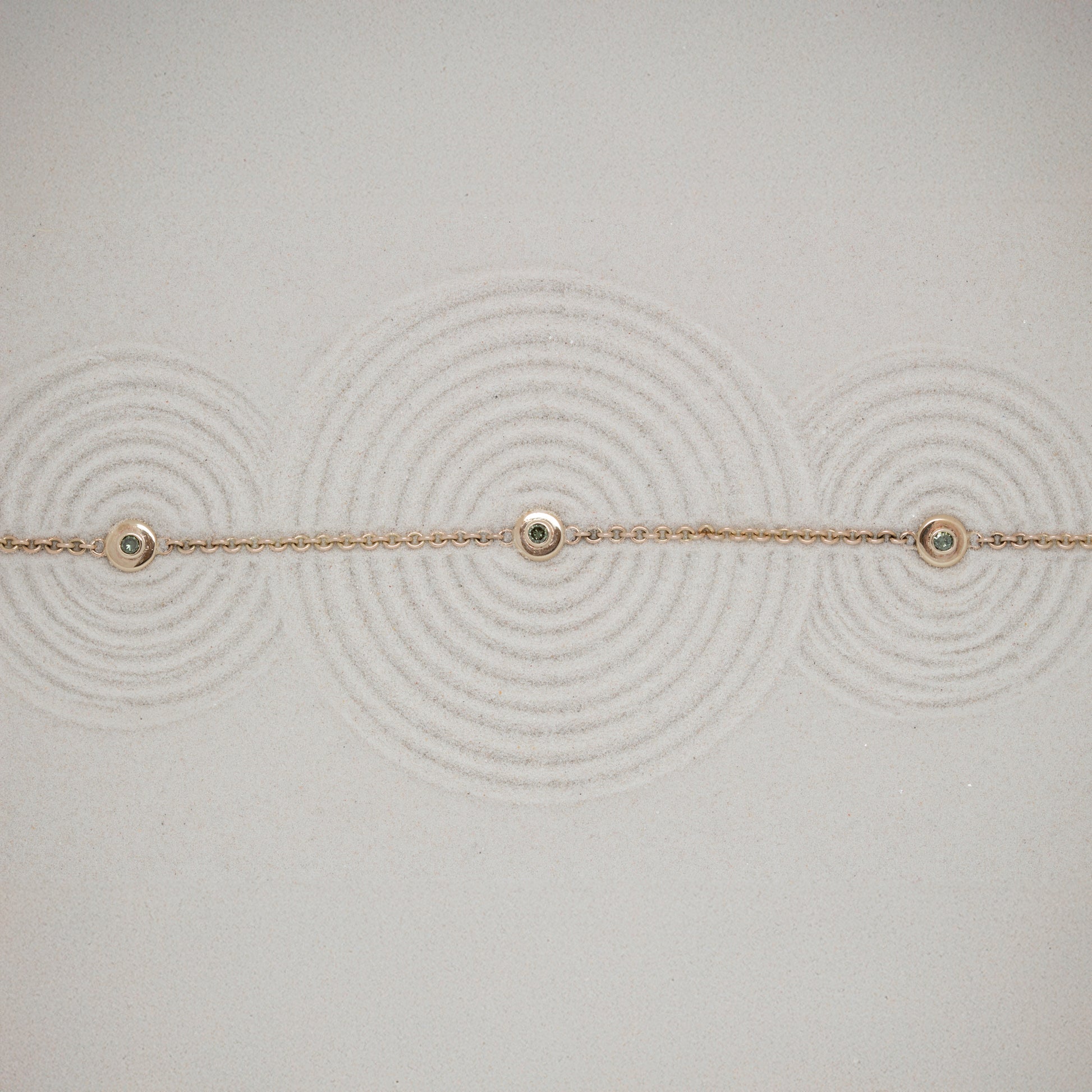 Delicate gold bracelet with small green diamonds on a textured sand background