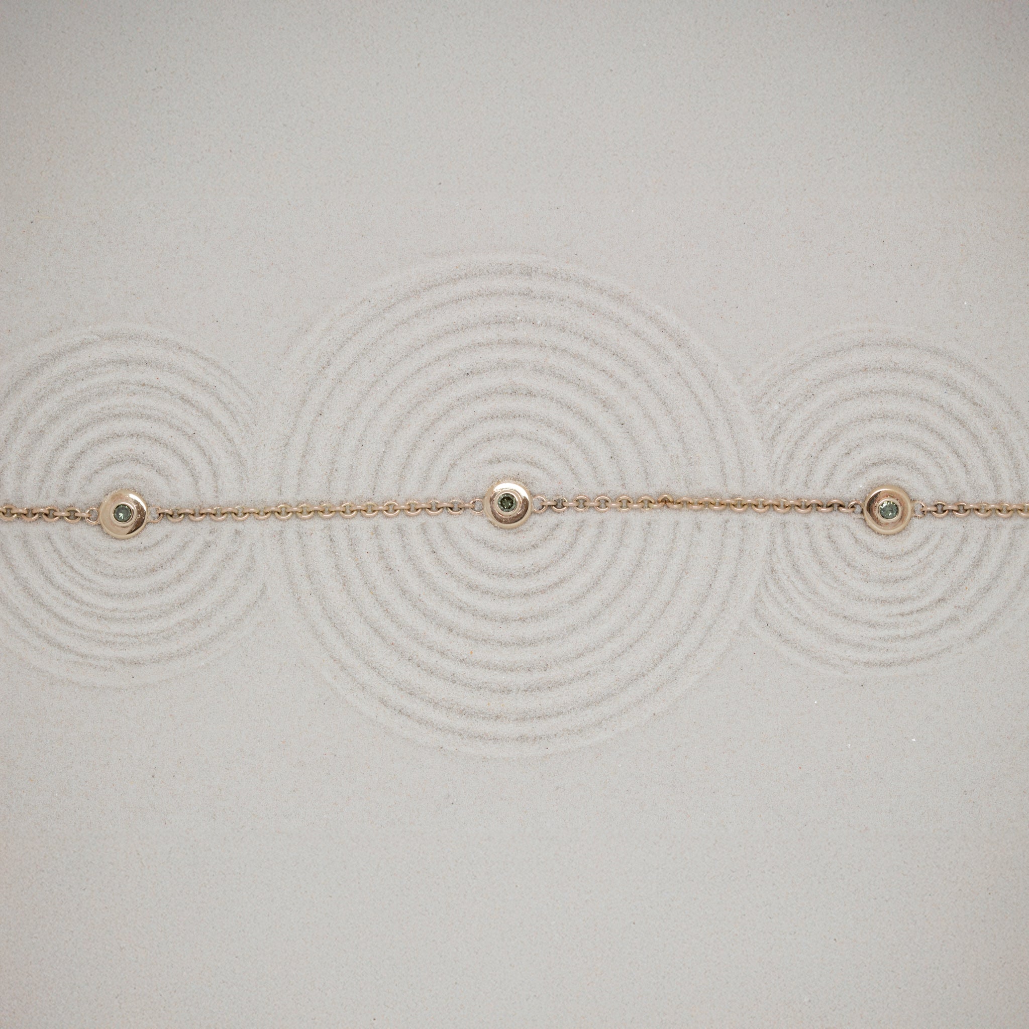 Delicate gold bracelet with small green diamonds on a textured sand background