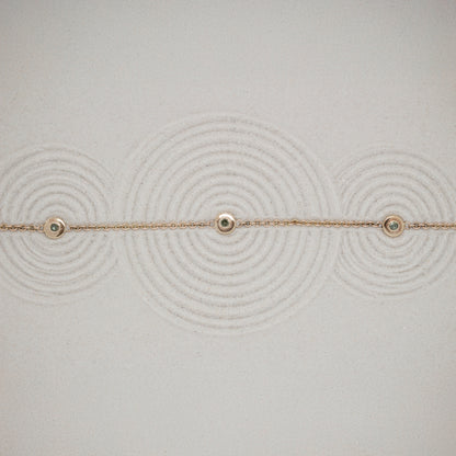 Delicate gold bracelet with small green diamonds on a textured sand background