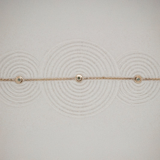Delicate gold bracelet with small green diamonds on a textured sand background