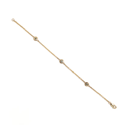 Gold bracelet with small round green diamond settings on a white background