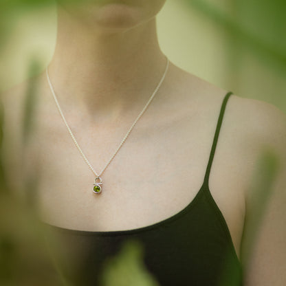 Person wearing a delicate necklace with a peridot pendant against a blurred natural background