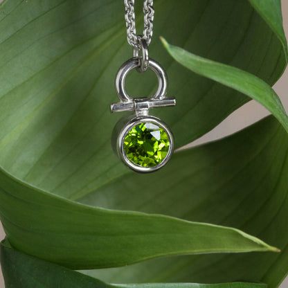 Silver necklace with a peridot gemstone pendant on a green leaf background