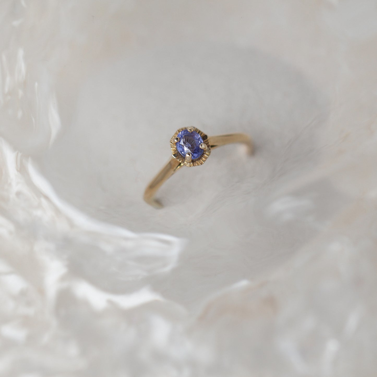 Gold ring with a sapphire gemstone on a textured beige background