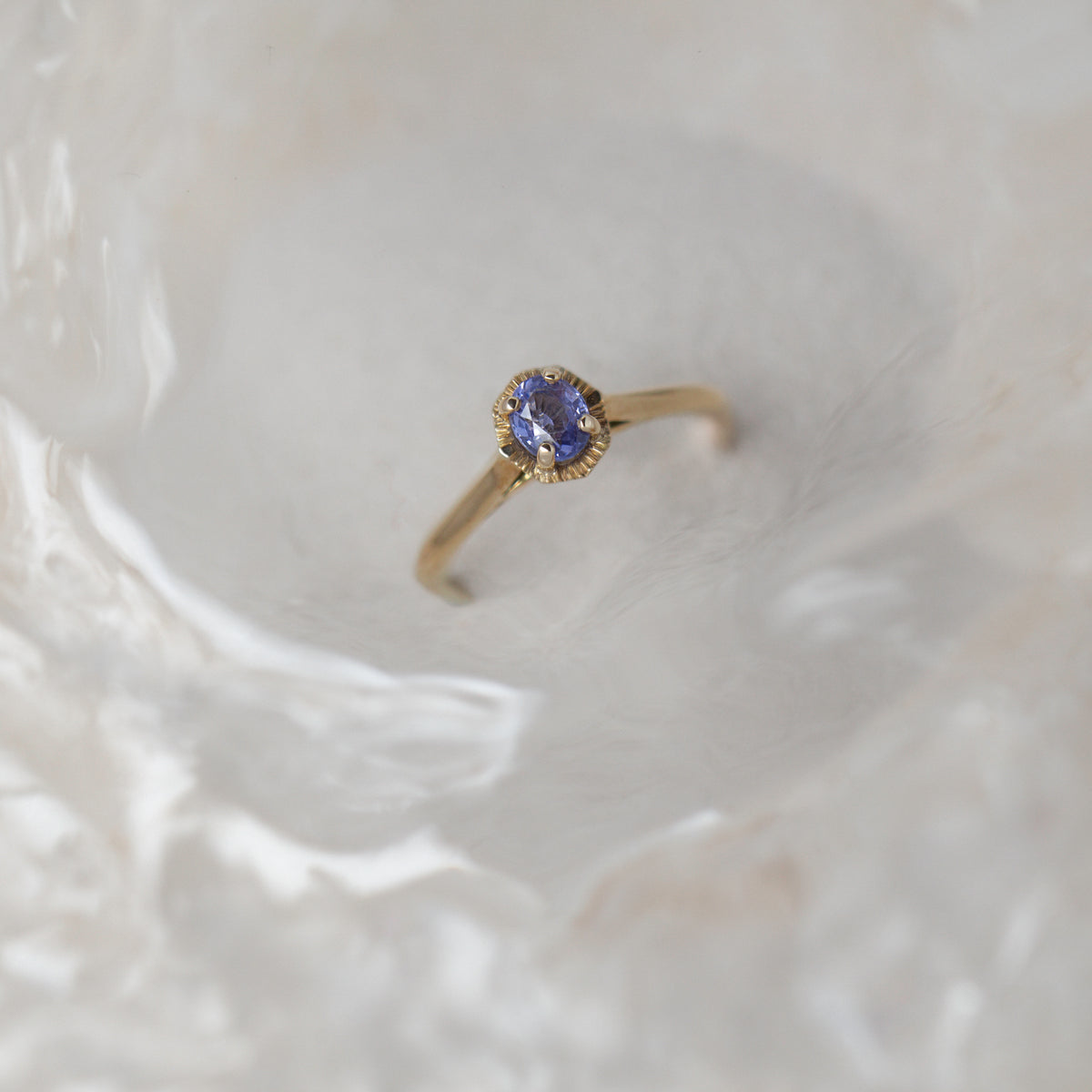 Gold ring with a sapphire gemstone on a textured beige background