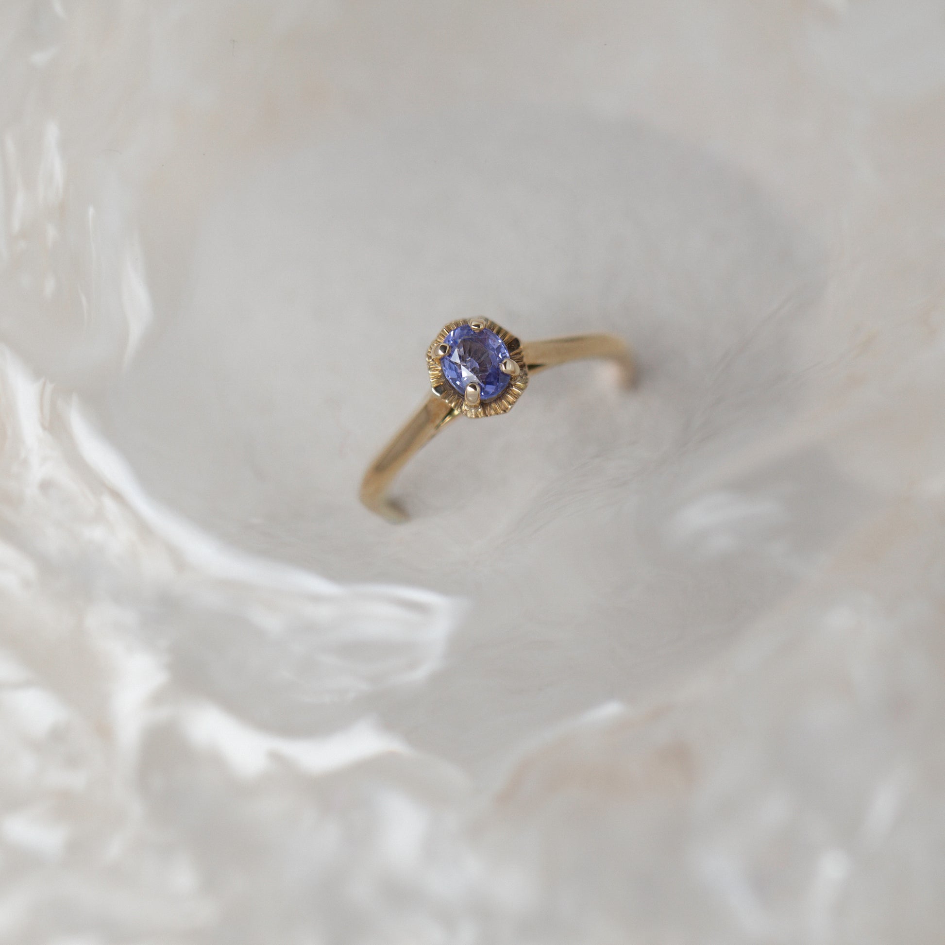 Gold ring with a sapphire gemstone on a textured beige background