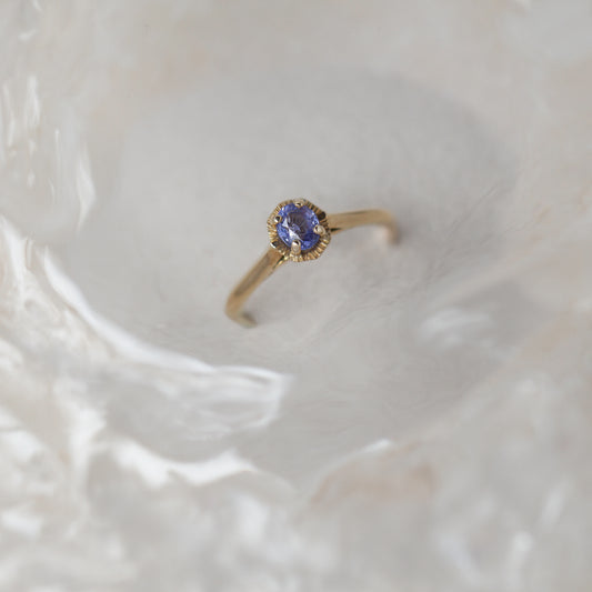 Gold ring with a sapphire gemstone on a textured beige background